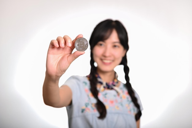 Portrait of beautiful happy young asian woman in denim dress holding crypto currency coin on white background