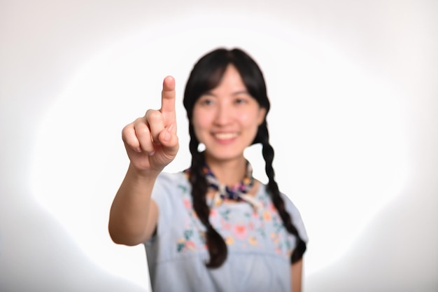 Portrait of beautiful happy young asian woman in denim dress touching invisible screen on white background