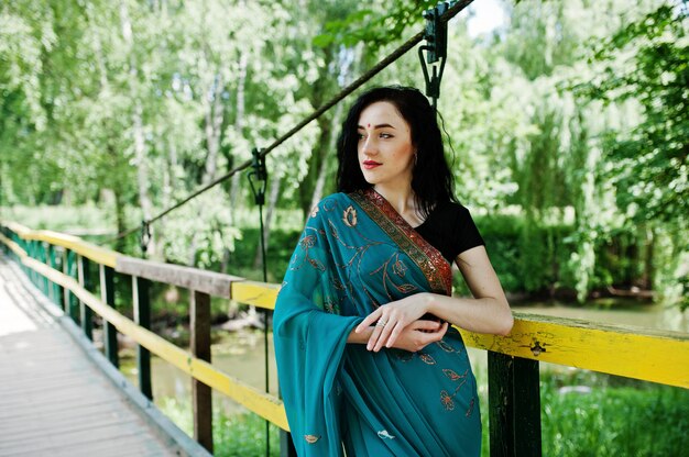 Portrait of beautiful indian brumette girl or hindu woman model on bridge. Traditional Indian costume lehenga choli.