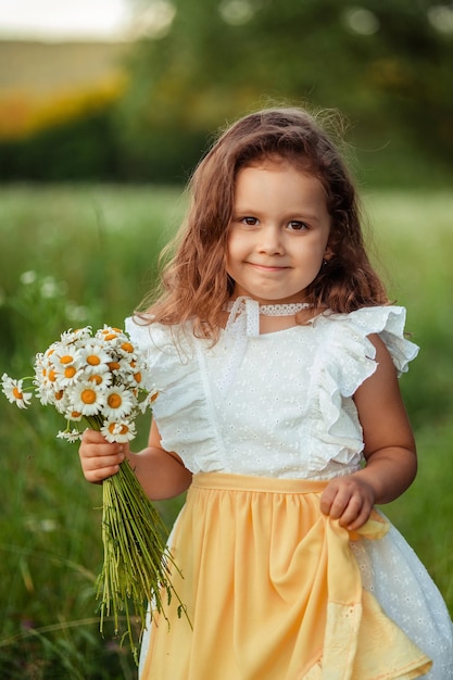 Portrait of a beautiful little girl 3 years old on a walk in the summer with a bouquet of daisies in her hands