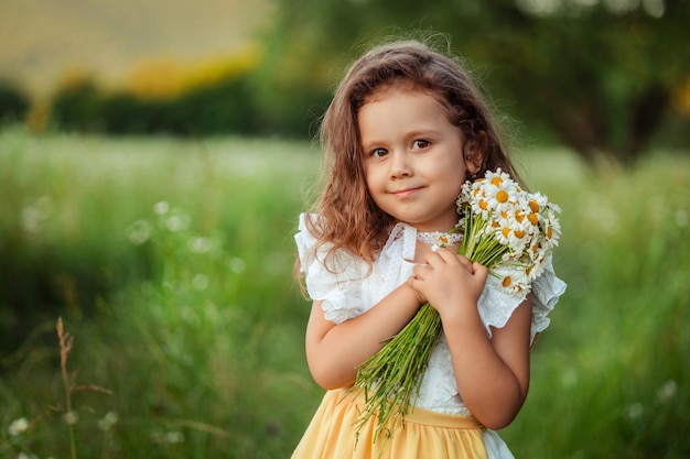 Portrait of a beautiful little girl 3 years old on a walk in the summer with a bouquet of daisies in her hands