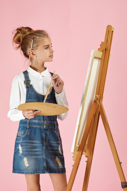 Portrait of beautiful little girl holding a wooden art palette and brush on studio background