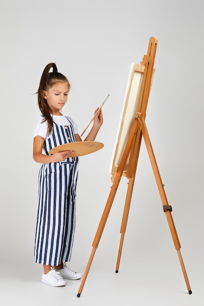 Portrait of beautiful little girl holding a wooden art palette and brush on studio background