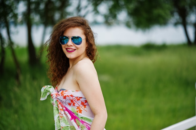 Portrait of a beautiful model posing against the fence in sunglasses in lakeside.