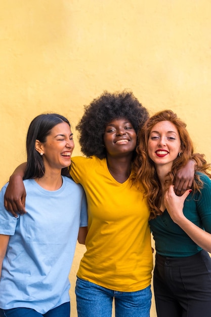 Portrait of beautiful multiethnic female friends smiling on a yellow wall having fun copy paste