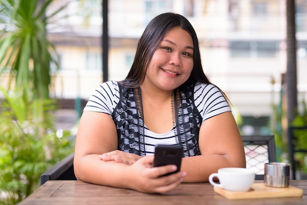 Portrait of beautiful overweight Asian woman relaxing at the coffee shop