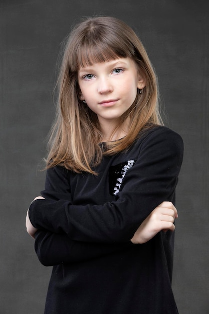 Portrait of a beautiful pensive girl of ten years old on a gray background