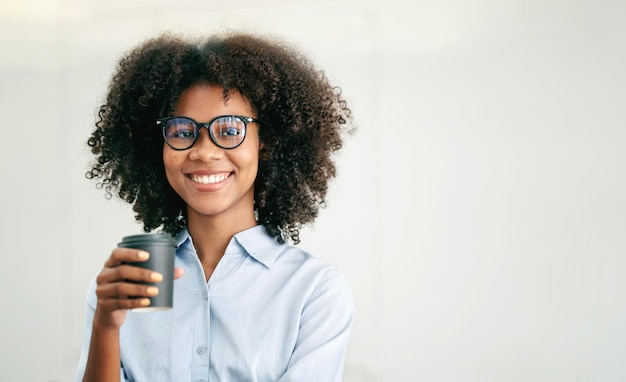 Portrait of beautiful positive african american woman with glasses holdng cup standing on white background