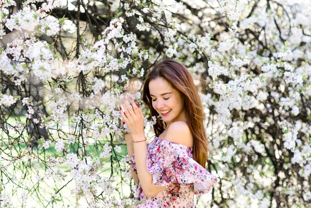 Portrait of beautiful red-haired young woman in white dress in spring flowers, blossom