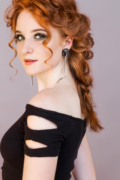 Portrait of a beautiful redhaired girl with long earrings Girl looking at the camera and posing on a gray background