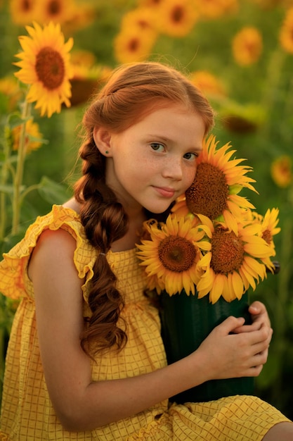 Portrait of a beautiful redhaired girl with pigtails with a bouquet of sunflowers in her hands summer in the village a field of sunflowers