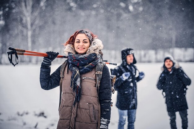 Portrait of a beautiful redhead girl with a backpack walking with his friends through a winter woods