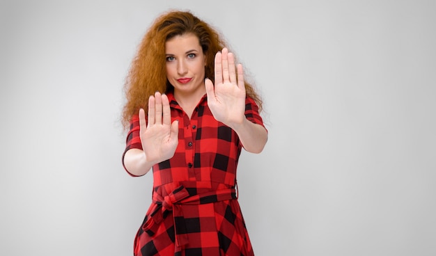 Portrait of beautiful redhead upset frustrated sad young woman showing stop sign on gray 