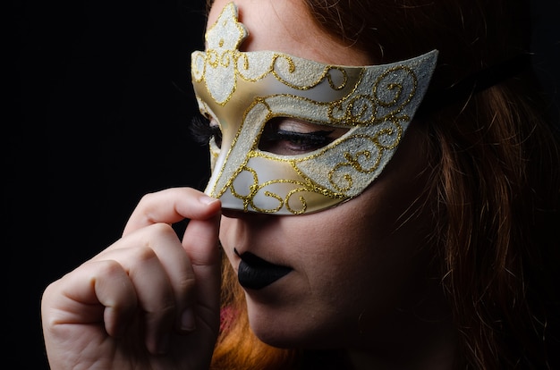 Portrait of a beautiful redhead with a Venetian mask done in a studio, low key image, with black background.