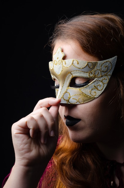 Portrait of a beautiful redhead with a Venetian mask done in a studio, low key image, with black background.