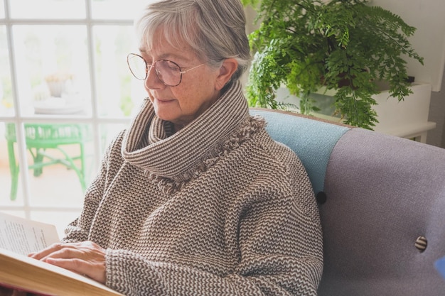 Portrait of beautiful relaxed senior woman sitting at home reading a book, retirement concept