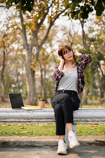 Portrait of beautiful and relaxed young Asian female college student sits on a bench in park