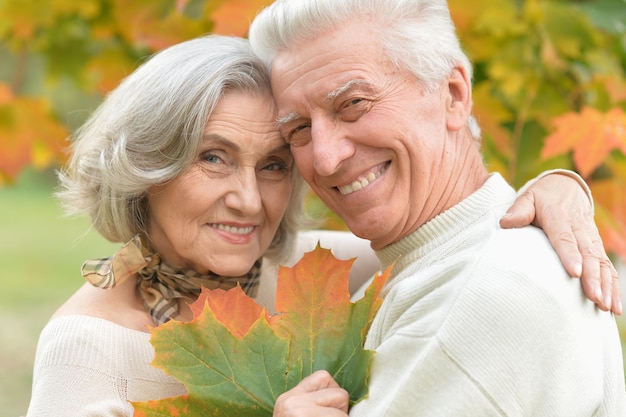 Portrait of beautiful senior couple in autumn park with leaves