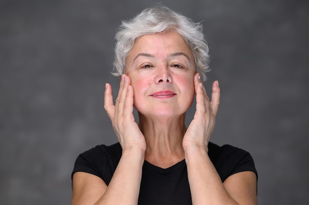 Portrait of beautiful senior woman gently applying under eye face cream elderly lady makes her skin ...