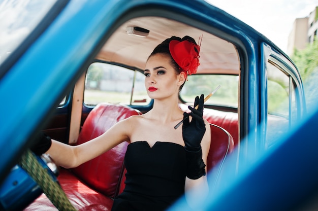 Portrait of beautiful sexy fashion girl model with bright makeup in retro style sitting in vintage car with a cigarette in hand.