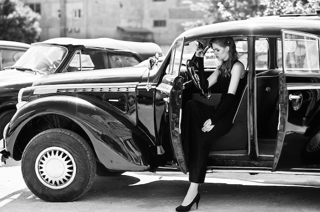 Portrait of beautiful sexy fashion girl model with bright makeup in retro style sitting in vintage car with a cigarette in hand.