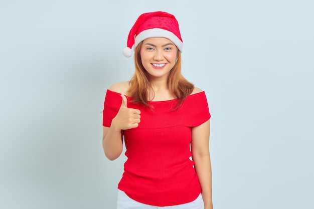 Portrait of beautiful smiling Asian woman wearing christmas dress and showing thumbs up or sign of approval on white background