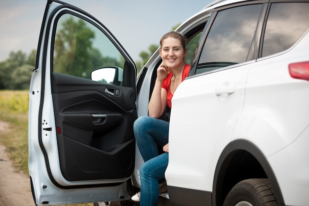 Portrait of beautiful smiling female driver relaxing in car at the field