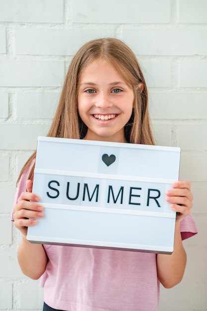 Portrait of a beautiful smiling little teenage girl against a white brick wall