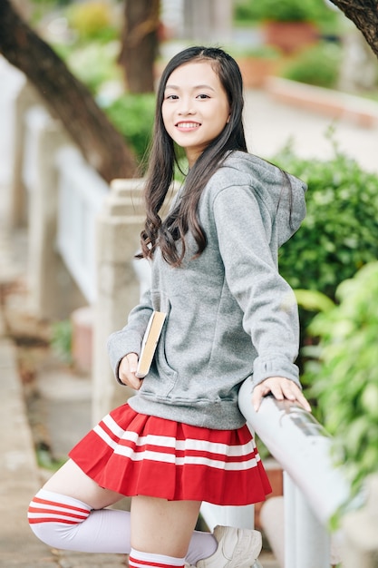 Portrait of beautiful smiling teenage Asian girl posing in park with book or dairy in hands