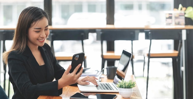 Portrait of beautiful smiling young entrepreneur businesswoman using smartphone and working on digital tablet in modern office room