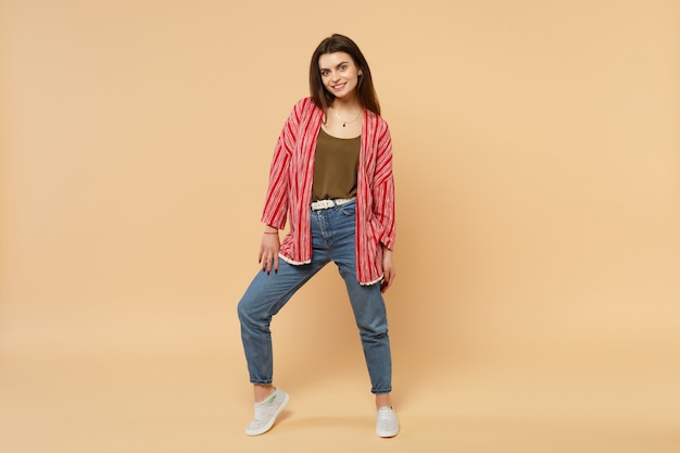 Portrait of beautiful smiling young woman in casual clothes standing looking camera isolated on pastel beige wall background in studio. People sincere emotions, lifestyle concept. Mock up copy space.