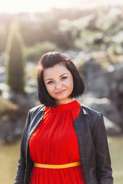 Portrait of a beautiful smiling young woman in nature in a red dress. A look at the camera