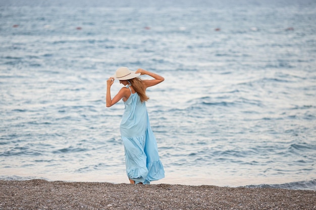 Portrait of beautiful smiling young woman wearing straw hat at beach with sea in background Beauty fashion girl looking at camera at seaside Carefree tanned woman walking on sand and laughing