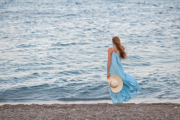 Portrait of beautiful smiling young woman wearing straw hat at beach with sea in background Beauty fashion girl looking at camera at seaside Carefree tanned woman walking on sand and laughing