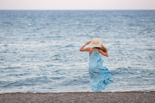 Portrait of beautiful smiling young woman wearing straw hat at beach with sea in background Beauty fashion girl looking at camera at seaside Carefree tanned woman walking on sand and laughing