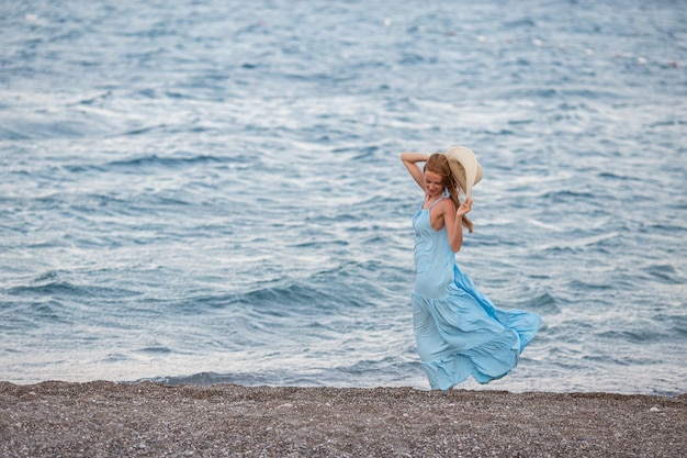 Portrait of beautiful smiling young woman wearing straw hat at beach with sea in background Beauty fashion girl looking at camera at seaside Carefree tanned woman walking on sand and laughing