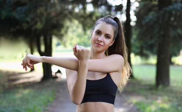 Portrait of beautiful sports woman stretches arms in park