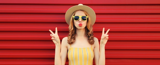 Photo portrait of beautiful stylish young woman in summer hat yellow sunglasses posing on red background