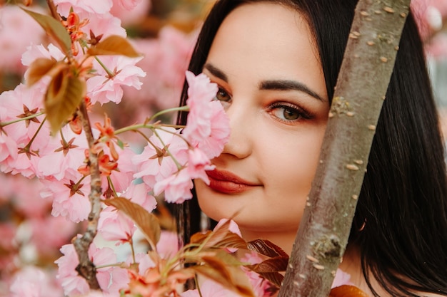 Portrait of beautiful tender woman dressed pink flowery dress posing near sakura cherry blossoms