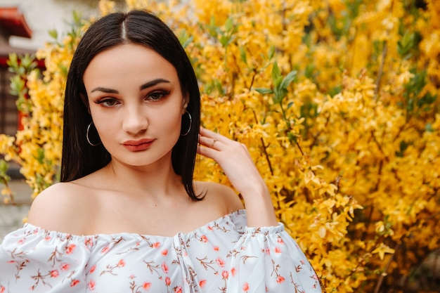 Portrait of beautiful tender woman dressed pink flowery dress posing near yellow forsythia tree