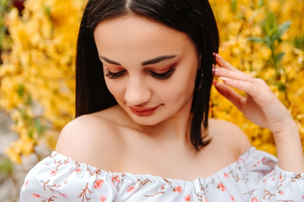 Portrait of beautiful tender woman dressed pink flowery dress posing near yellow forsythia tree