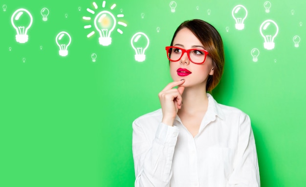 Portrait of beautiful thoughtful young woman in glasses with abstract  bulbs on the studio green background