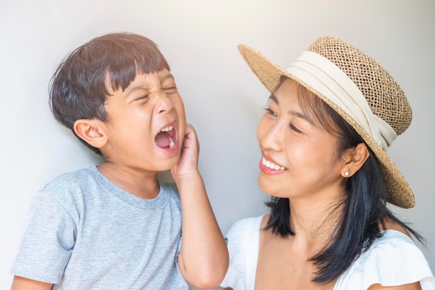 Portrait beautiful traveler asian mother in white dress straw hat and son in grey shirt enjoys relax smile leisure at resort in tropical beach vacation