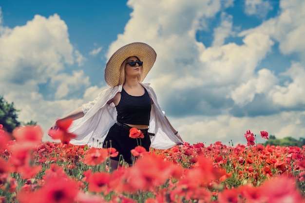 Portrait of beautiful ukrainian woman with blond hair, wearing white blouse, posing in poppy field at sunny day, lifestyle