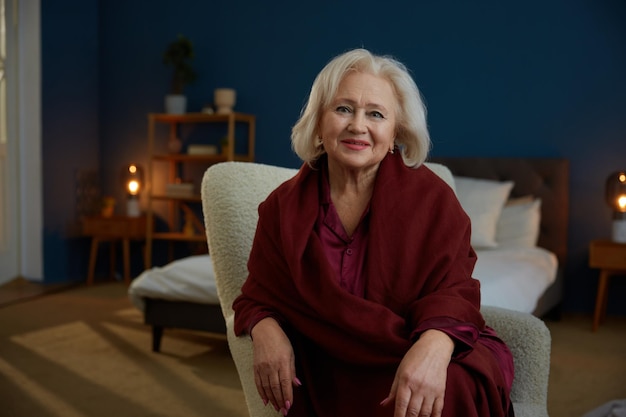 Portrait of beautiful wellgroomed senior woman sitting on armchair at home