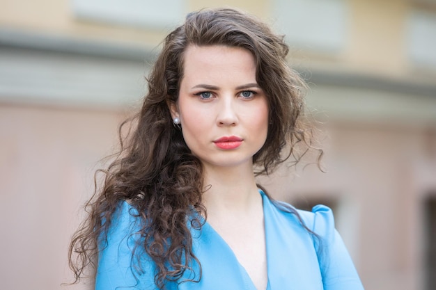 Portrait of a beautiful white European brunette girl wearing a blue dress on the street in the summe