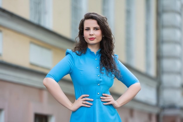 Portrait of a beautiful white European brunette girl wearing a blue dress on the street in the summe