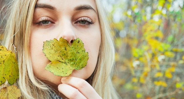 Portrait of beautiful woman covering her mouth with autumn yellow leaf