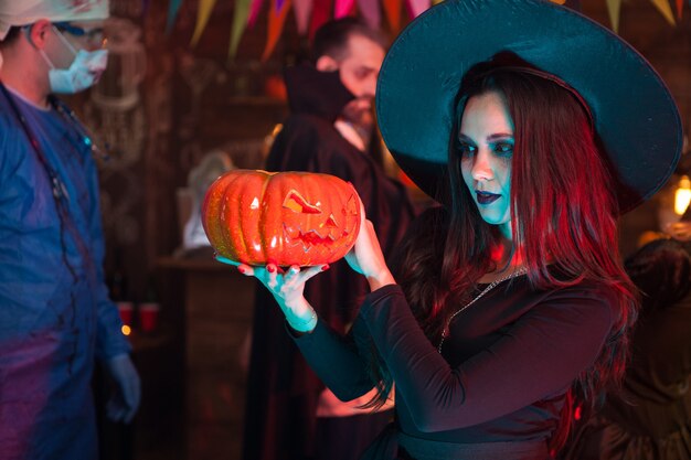 Photo portrait of beautiful woman dressed up like a witch doing dark magic on a pumpkin for halloween. dracula at halloween party.