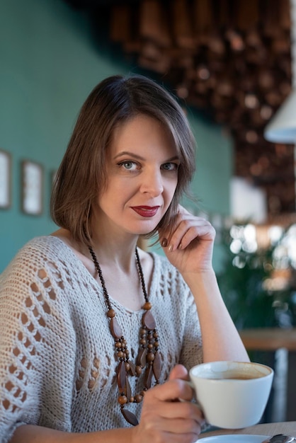 Portrait of beautiful woman drinks coffee on inside cafe Portrait of brunette girl sits at table in cafe